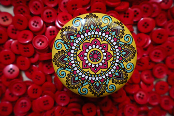 Relaxing and easy mandala design on a yellow pot with red sewing button at background.
