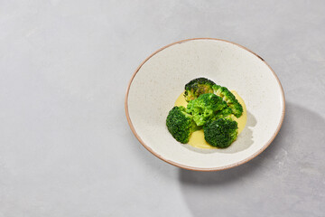 Broccoli with cheese sauce on a speckled plate, minimalistic composition, natural daylight, soft neutral background