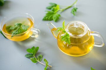 Tea in a glass teapot and cup with currant and mint leaves
