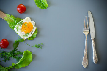 Appetizing fried egg with greens on wooden spatula, on gray background