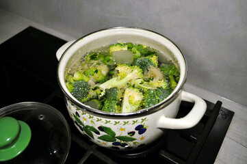 white pan on an induction stove with soup made from pieces of broccoli, cabbage, cauliflower,...
