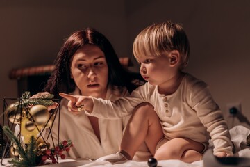 Curious toddler points with wonder as mother listens closely sharing a quiet moment of discovery warmth during cozy family holiday evening The atmosphere is warm and intimate, suggesting a moment