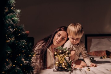 Mother and son rest their heads together watching Christmas decor in peaceful shared stillness full of warmth intimacy and quiet attention to gentle holiday moments