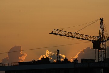 Sanset over city with silhouette of construction crane and building.