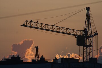 Obraz premium Sanset over city with silhouette of construction crane and building.