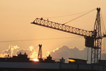 Obraz premium Sanset over city with silhouette of construction crane and building.