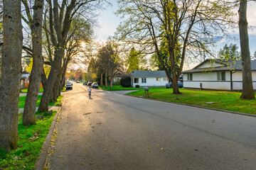 A young boy rides a bicycle down a tree lined residential street in the historic Sanders Beach neighborhood of Coeur d'Alene, Idaho at dusk.
