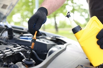 Worker checking motor oil level in car with dipstick, closeup