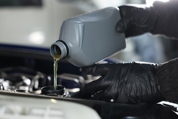 Worker pouring motor oil from canister into car engine, closeup