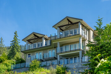 Top of grey stucco luxury house with shingle roof, green trees and nice windows in Spring in...