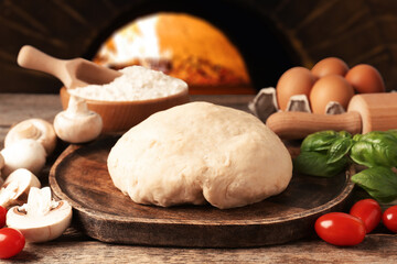 Fresh ingredients for pizza on wooden table against oven