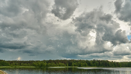 Grey rainy clouds over the lake. Dense forest along the lake shore during a storm.