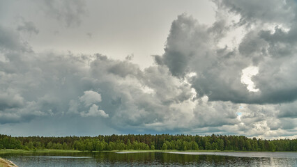Grey rainy clouds over the lake. Dense forest along the lake shore during a storm.