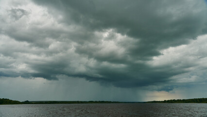 Grey rainy clouds over the lake. Dense forest along the lake shore during a storm.