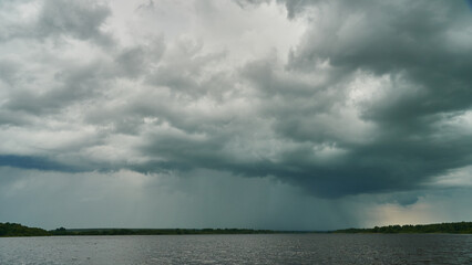 Grey rainy clouds over the lake. Dense forest along the lake shore during a storm.