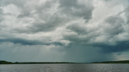 Grey rainy clouds over the lake. Dense forest along the lake shore during a storm.