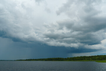 Grey rainy clouds over the lake. Dense forest along the lake shore during a storm.