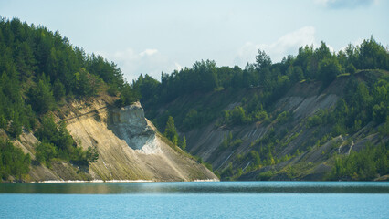 An old abandoned sand quarry. The shore of the quarry is overgrown with forest. Extraction of sand and stone for industrial applications.