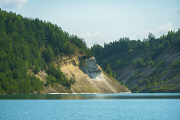 An old abandoned sand quarry. The shore of the quarry is overgrown with forest. Extraction of sand and stone for industrial applications.