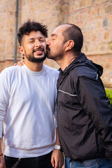 Mature bald man couple and young curly haired gay geek showing their love outdoors at sunset for...
