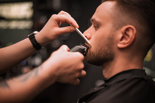 Close-up of a barber trimming a client's mustache with electric clippers and a comb, showcasing precise grooming technique and personal care in a modern barbershop setting..