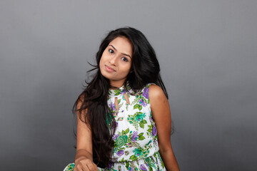 A confident young woman wearing a floral top poses gracefully in a studio setting, showcasing...