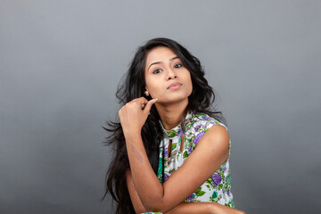 A confident young woman wearing a floral top poses gracefully in a studio setting, showcasing...