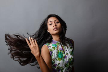 A confident young woman wearing a floral top poses gracefully in a studio setting, showcasing...