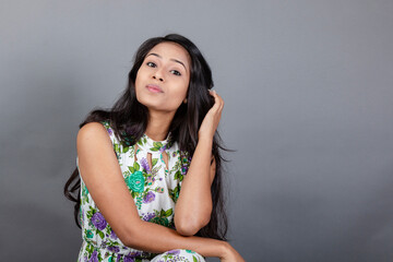 A confident young woman wearing a floral top poses gracefully in a studio setting, showcasing...