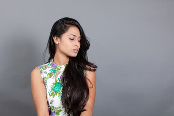 A confident young woman wearing a floral top poses gracefully in a studio setting, showcasing...