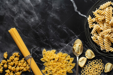 Different types of pasta lie side by side against a dark background with a marbled texture. You can...