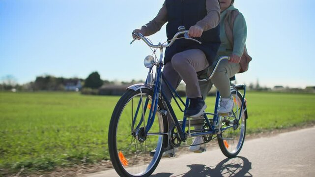 Sporty elderly couple on a two-seater bicycle takes a ride through a countryside
