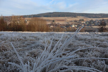 Frost-Covered Field with Village and Hills in Winter Light