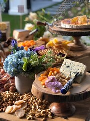 Elegant Cheese Board with Dried Fruit, Nuts, and Floral Garnishes at an Outdoor Event”