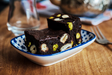 close up of chocolate brownie on plate in cafe, delicious chocolate dessert bar with hazelnuts and pistachios, selective focus on dessert, popular in restaurants, ice cream parlors and coffee houses