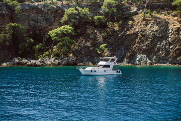 White yacht anchored in crystal-clear waters near rocky coastline