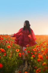 Sexy girl in short red dress posing on poppy field of flowers.