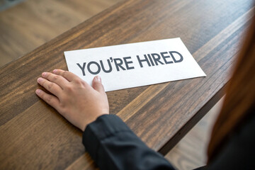 Close up of a hand reaching for youre hired message on a wooden table