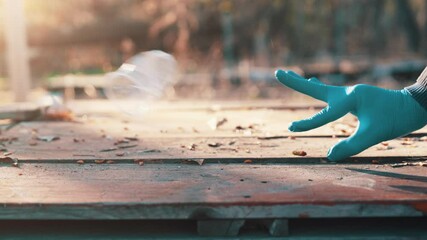 Hand in blue latex glove flicking crumpled plastic cup with finger snap off wooden picnic table slow motion spring sunset