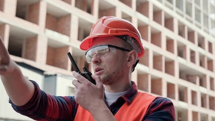 Foreman in protective helmet communicating on two-way radio on site