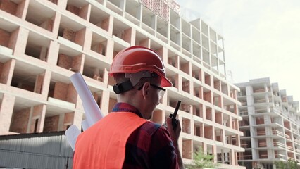 Foreman with drawings in hand talking on walkie-talkie on site