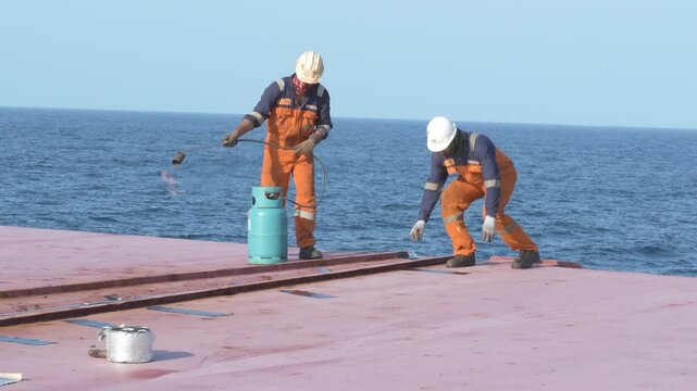 crew members fixing hatch sealing tape on cargo pontoon top openings by heating up surface and tape for cargo protection 