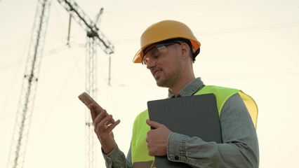 Pleased energy auditor having phone conversation near electricity pylon