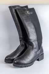Stylish black leather knee-high boots with silver buckle and textured elastic side panel.
