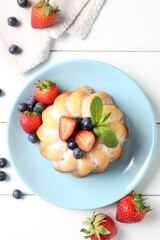 Tasty Bundt cake with powdered sugar and berries on white wooden table, flat lay