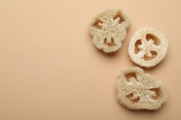 Natural loofah sponges on beige background, flat lay. Space for text
