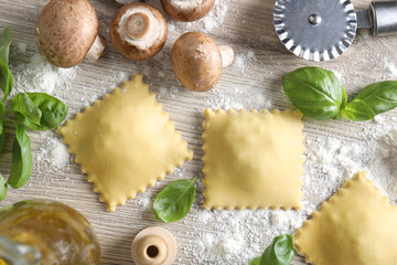 Uncooked ravioli, mushrooms, basil and cutter on white wooden table, flat lay