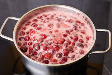 Bubbling red strawberry berries create a vibrant mixture as they simmer in a pot.