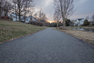 Suburban asphalt path, with pond and houses, at dusk