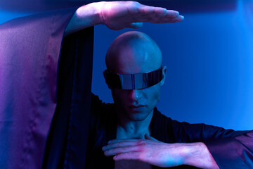 Black and white image of a man in a stylish outfit, showcasing a confident pose with futuristic sunglasses in an artistic setting.